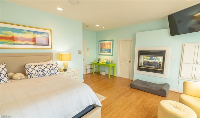 bedroom with a multi sided fireplace and light wood-type flooring