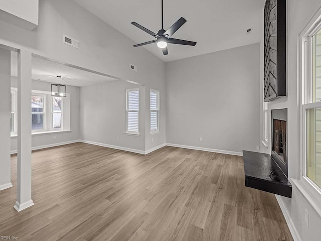 unfurnished living room with lofted ceiling, ceiling fan with notable chandelier, a fireplace, and light wood-type flooring