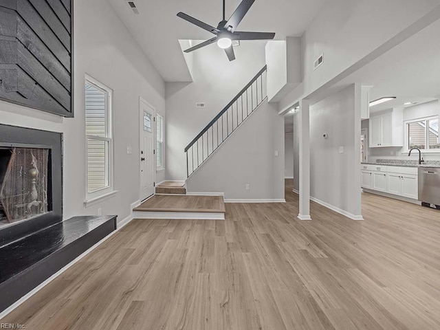 unfurnished living room with a towering ceiling, ceiling fan, and light hardwood / wood-style flooring