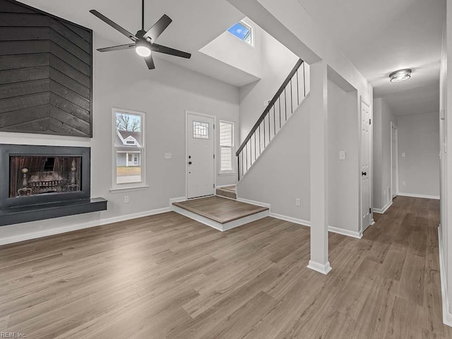 entryway featuring ceiling fan, a large fireplace, light hardwood / wood-style floors, and a towering ceiling