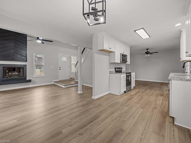 kitchen with white cabinetry, a large fireplace, appliances with stainless steel finishes, ceiling fan, and light stone countertops