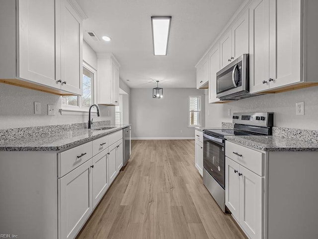 kitchen with light hardwood / wood-style flooring, white cabinetry, stainless steel appliances, light stone countertops, and decorative light fixtures