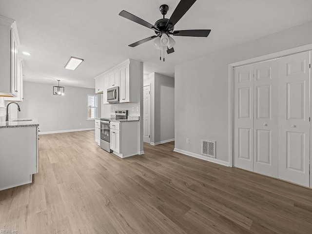 kitchen with pendant lighting, white cabinetry, sink, stainless steel appliances, and light wood-type flooring