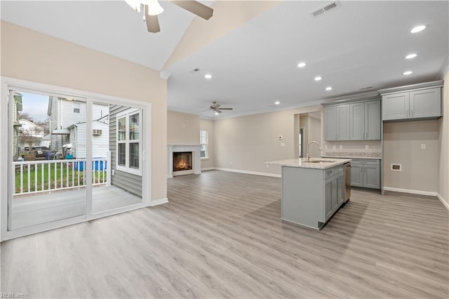 kitchen with an island with sink, gray cabinetry, ceiling fan, light hardwood / wood-style floors, and light stone countertops