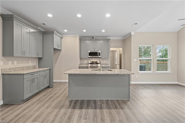 kitchen with light stone counters, stainless steel appliances, gray cabinets, and a center island with sink