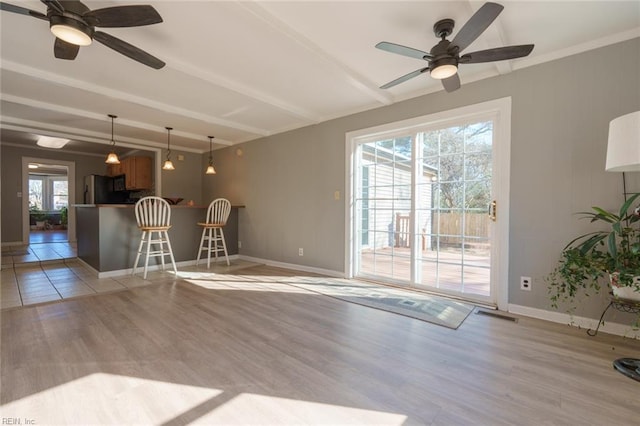 unfurnished living room featuring beamed ceiling, ceiling fan, and light wood-type flooring