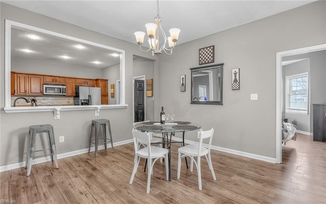 dining space with light wood-type flooring, baseboards, and a notable chandelier