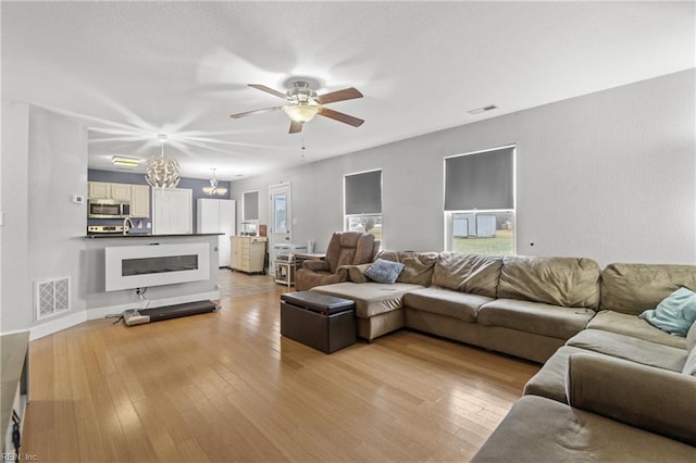 living room featuring ceiling fan with notable chandelier and light hardwood / wood-style flooring