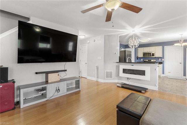 living room with sink, ceiling fan with notable chandelier, and light hardwood / wood-style flooring