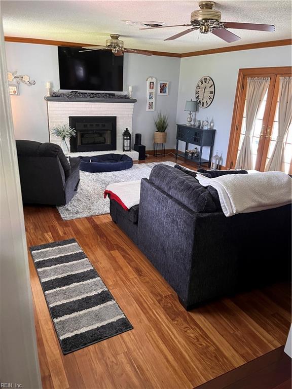 living room featuring crown molding, ceiling fan, hardwood / wood-style floors, a textured ceiling, and a brick fireplace