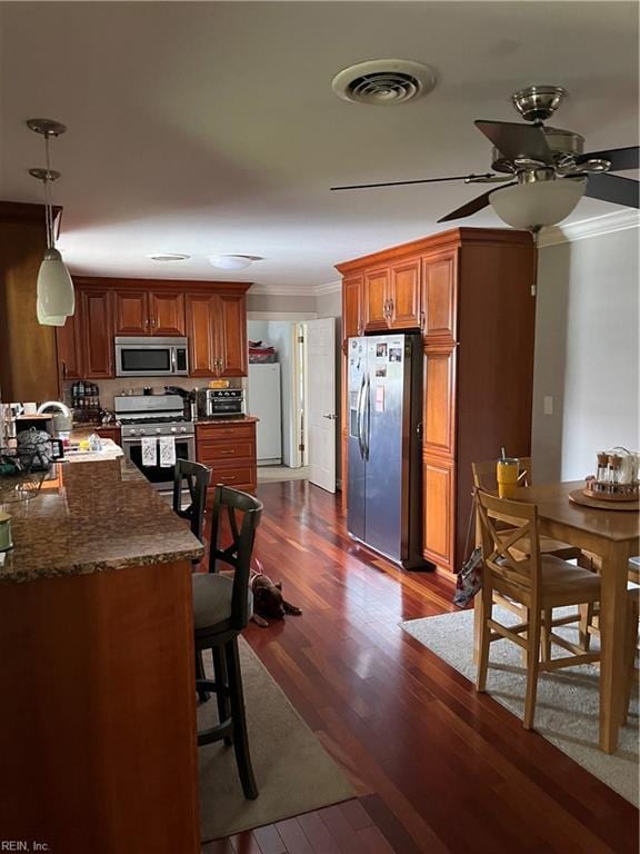 kitchen with dark stone countertops, hanging light fixtures, stainless steel appliances, dark hardwood / wood-style floors, and ornamental molding