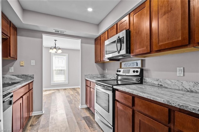 kitchen featuring stainless steel appliances, light stone countertops, pendant lighting, and light wood-type flooring