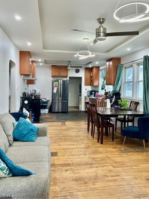 interior space featuring stainless steel refrigerator, pendant lighting, a raised ceiling, and light wood-type flooring