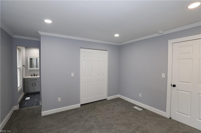 unfurnished bedroom with sink, ensuite bath, dark colored carpet, ornamental molding, and a closet