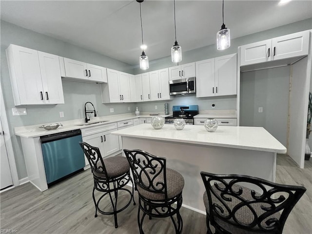 kitchen featuring sink, appliances with stainless steel finishes, white cabinets, a kitchen island, and decorative light fixtures