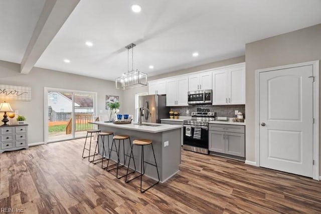 kitchen featuring appliances with stainless steel finishes, white cabinets, a kitchen breakfast bar, hanging light fixtures, and a kitchen island with sink