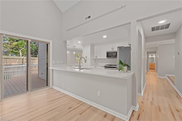 kitchen featuring appliances with stainless steel finishes, light wood-type flooring, white cabinets, sink, and kitchen peninsula