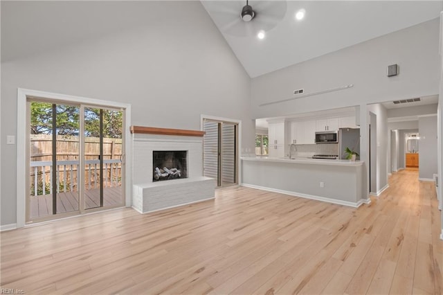 unfurnished living room with ceiling fan, light hardwood / wood-style floors, high vaulted ceiling, sink, and a brick fireplace