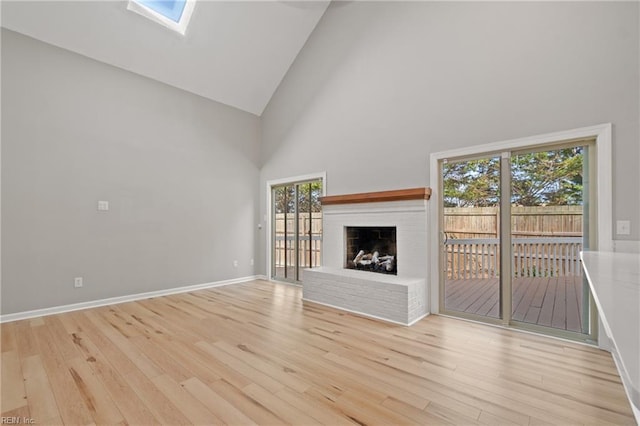 unfurnished living room with light hardwood / wood-style floors, high vaulted ceiling, a skylight, and a fireplace