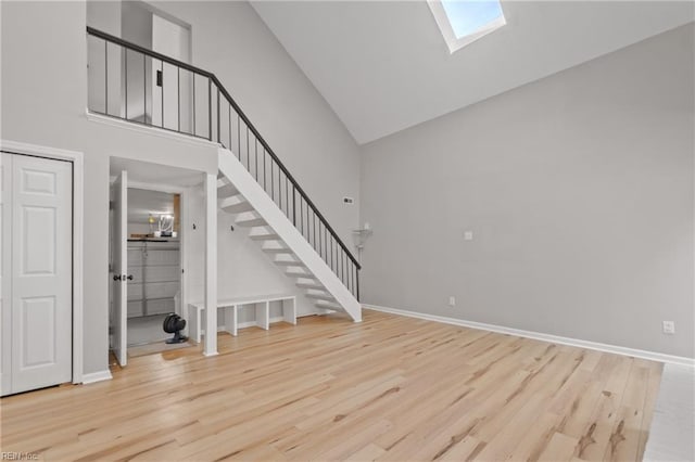 unfurnished living room featuring hardwood / wood-style floors, high vaulted ceiling, and a skylight