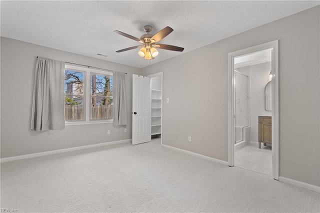 unfurnished bedroom with ceiling fan, a textured ceiling, a walk in closet, and light colored carpet