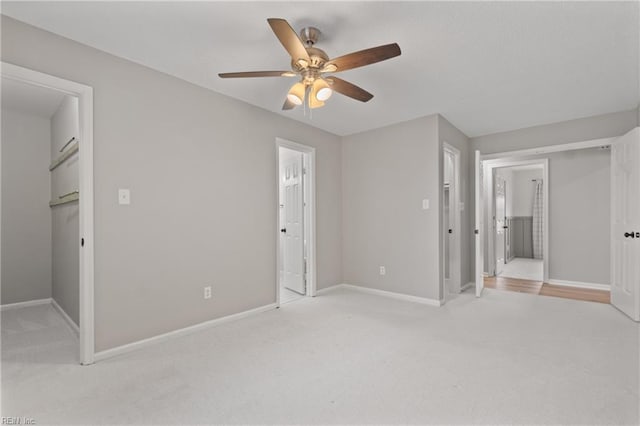 unfurnished bedroom with light carpet, ceiling fan, a walk in closet, and ensuite bath