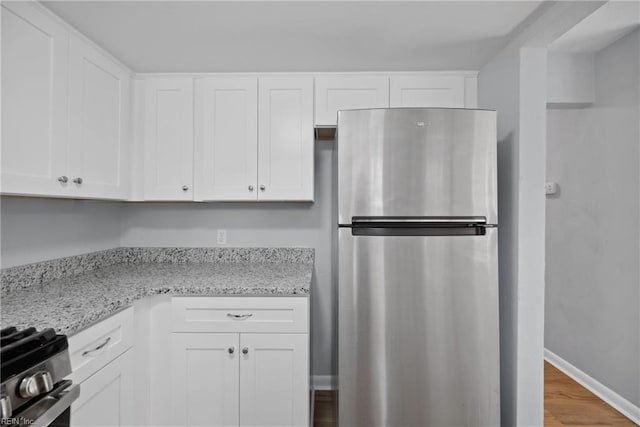 kitchen with stainless steel appliances, white cabinets, light stone counters, and light hardwood / wood-style floors