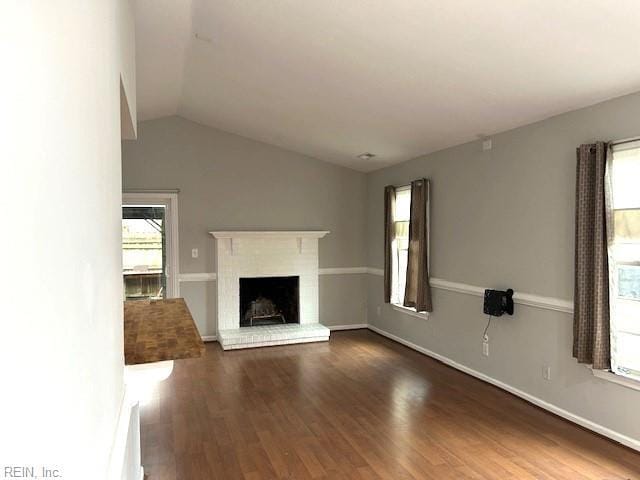 unfurnished living room featuring a brick fireplace, vaulted ceiling, baseboards, and wood finished floors