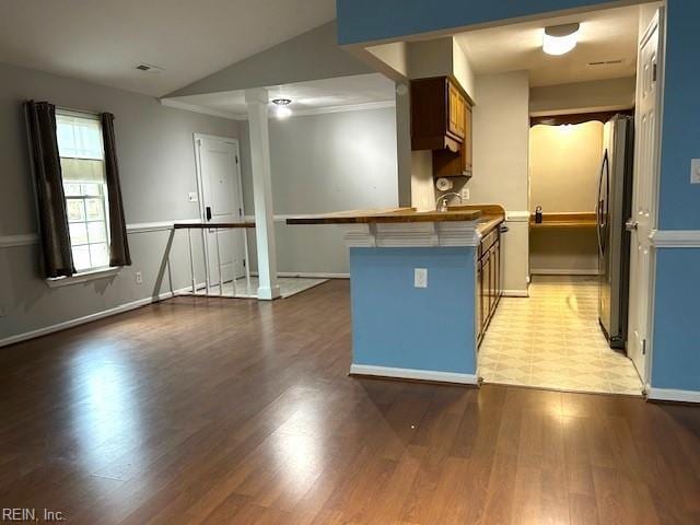 kitchen with a breakfast bar, lofted ceiling, stainless steel fridge, light hardwood / wood-style floors, and kitchen peninsula