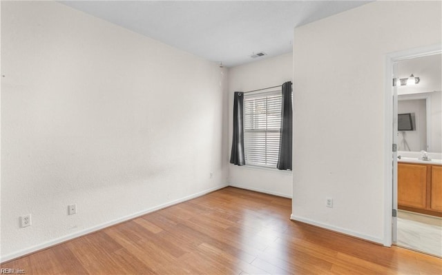 unfurnished bedroom featuring ensuite bathroom, sink, and light hardwood / wood-style flooring