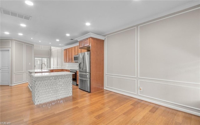 kitchen with sink, a center island, appliances with stainless steel finishes, light hardwood / wood-style floors, and backsplash