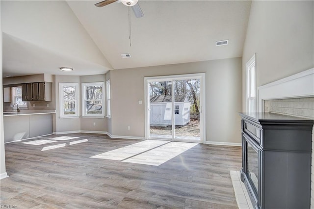 unfurnished living room with high vaulted ceiling, a healthy amount of sunlight, sink, and light wood-type flooring