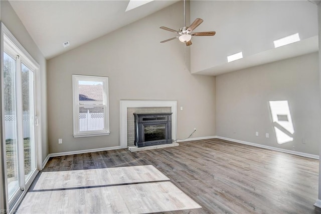 unfurnished living room with wood-type flooring, a skylight, high vaulted ceiling, a brick fireplace, and ceiling fan