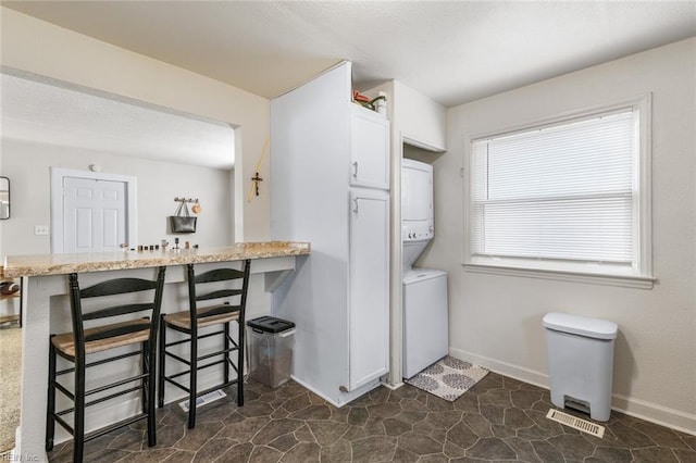 kitchen with stacked washer / drying machine, a breakfast bar area, white cabinets, and kitchen peninsula