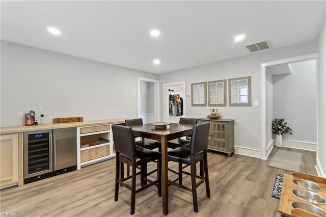 dining area with wine cooler, light hardwood / wood-style flooring, and indoor bar