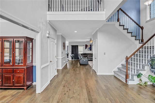 foyer entrance featuring a towering ceiling, light hardwood / wood-style flooring, ornamental molding, and ceiling fan