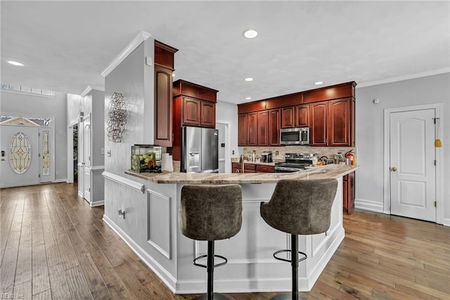 kitchen featuring dark hardwood / wood-style floors, a kitchen bar, ornamental molding, kitchen peninsula, and stainless steel appliances