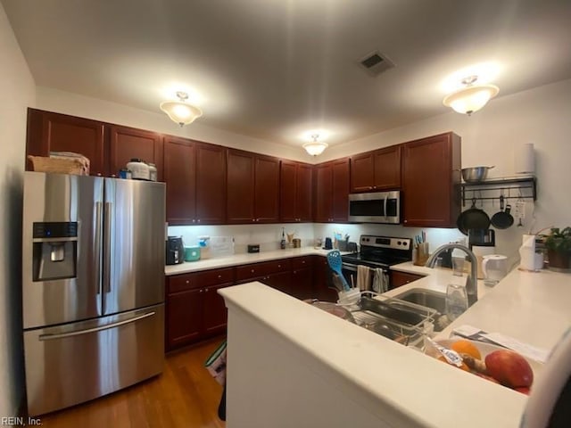 kitchen featuring visible vents, a peninsula, a sink, light countertops, and appliances with stainless steel finishes