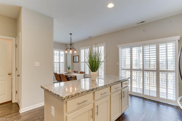 kitchen featuring dark wood-type flooring, a center island, light stone countertops, white cabinets, and decorative light fixtures