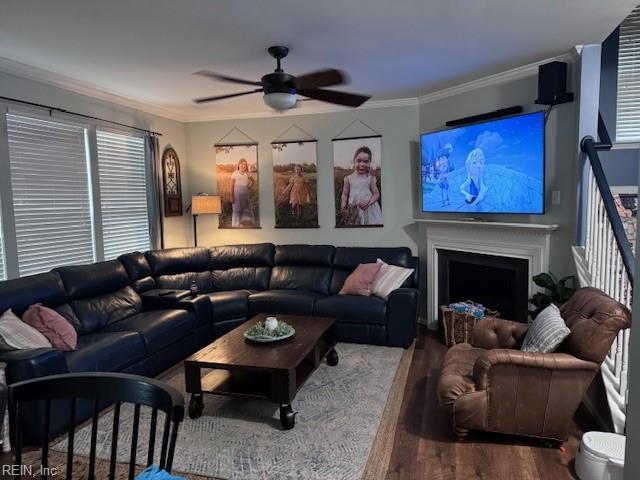 living area with ornamental molding, a fireplace, wood finished floors, and a ceiling fan