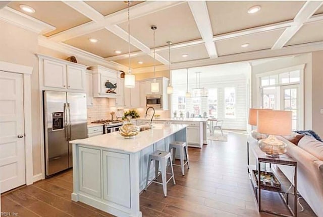 kitchen with white cabinetry, appliances with stainless steel finishes, a kitchen island with sink, and decorative light fixtures