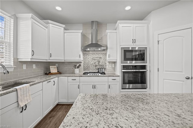 kitchen featuring white cabinetry, light stone countertops, sink, appliances with stainless steel finishes, and wall chimney exhaust hood