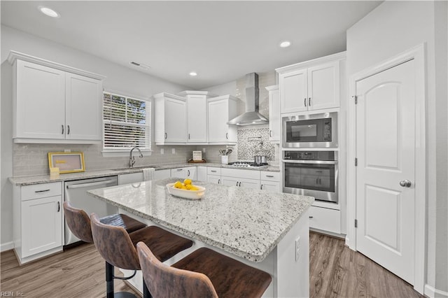 kitchen featuring appliances with stainless steel finishes, a kitchen breakfast bar, white cabinets, wall chimney range hood, and a kitchen island