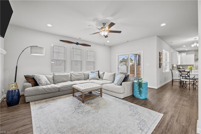 living room with ceiling fan with notable chandelier and dark hardwood / wood-style flooring