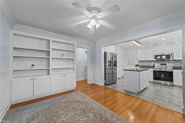 kitchen with appliances with stainless steel finishes, ornamental molding, white cabinets, ceiling fan with notable chandelier, and light wood-type flooring