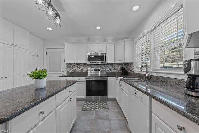 kitchen with white cabinetry, stainless steel appliances, sink, dark stone counters, and decorative backsplash