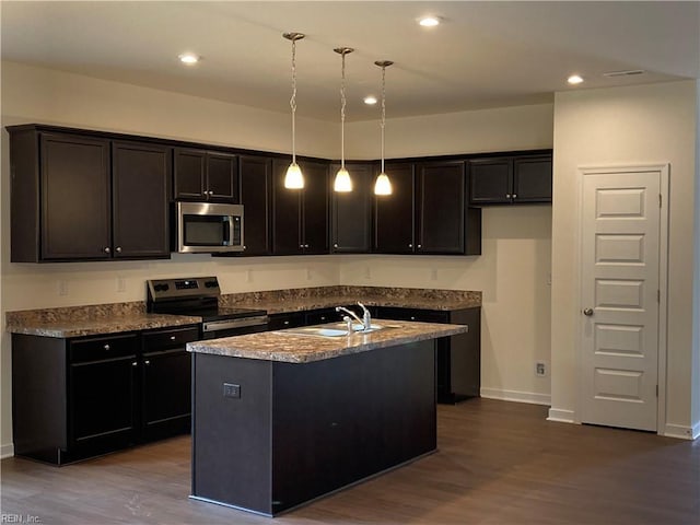 kitchen with hardwood / wood-style floors, sink, decorative light fixtures, stainless steel appliances, and an island with sink