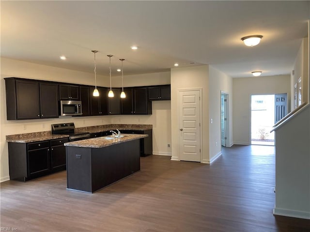 kitchen featuring appliances with stainless steel finishes, light stone countertops, pendant lighting, hardwood / wood-style floors, and a kitchen island with sink