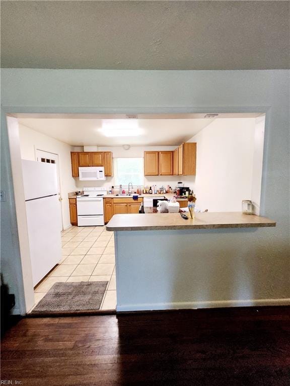 kitchen with sink, white appliances, kitchen peninsula, and light wood-type flooring