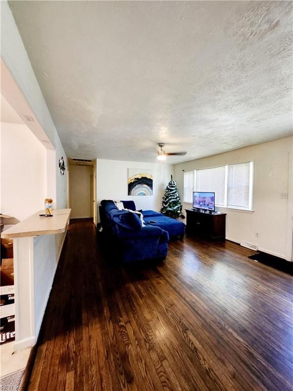 living room with dark hardwood / wood-style flooring, ceiling fan, and a textured ceiling